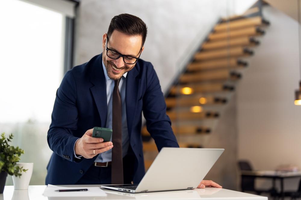 Hymyilevä yritysjohtaja lukemassa Luottopostin turvallista viestiä puhelimestaan toimistossaan.